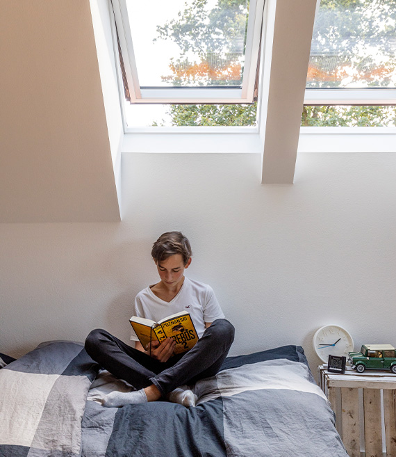 Tinejdžer čita knjigu u dječjoj sobi u potkrovlju.